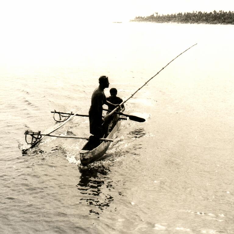 Black and white photo of people fishing on a small canoe.