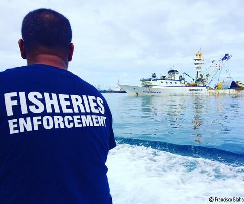 Back view of fisheries enforcement officer at sea with a boat in the background.